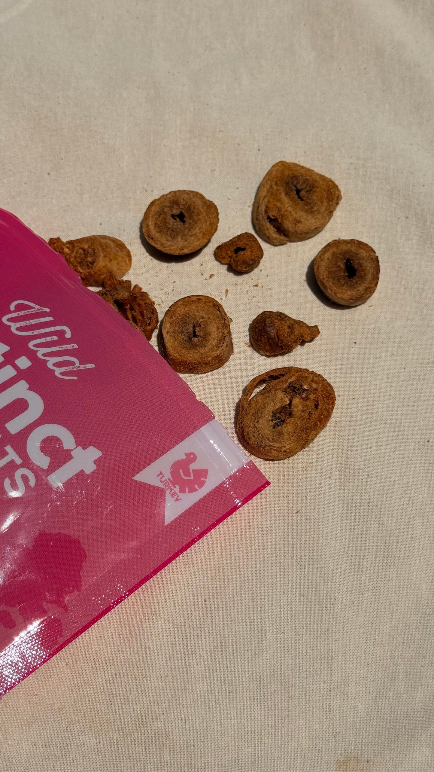Dog treats scattered on a beige surface next to a pink package with 'Wild Instinct' branding.