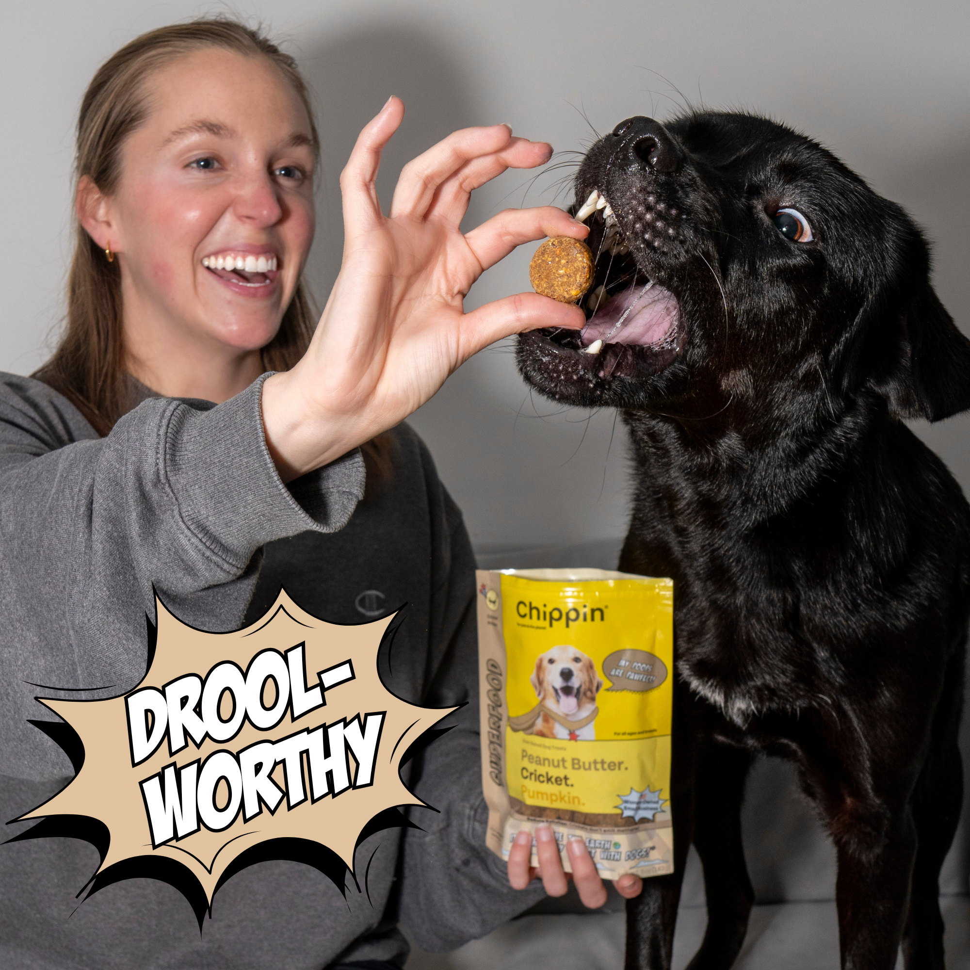 Woman feeding a black dog a treat with a 'Chippin' product in the background