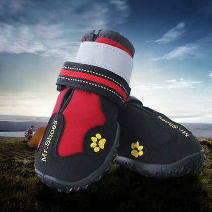 Red and black dog shoes with paw prints on a grassy field with a tent and person in the background.
