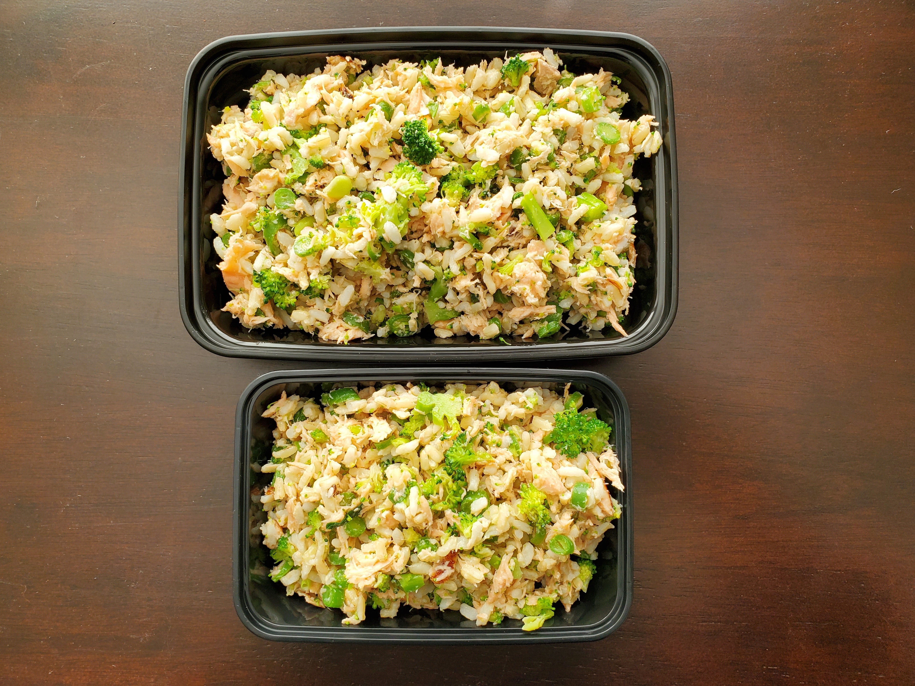 Two containers of rice and broccoli on a wooden surface