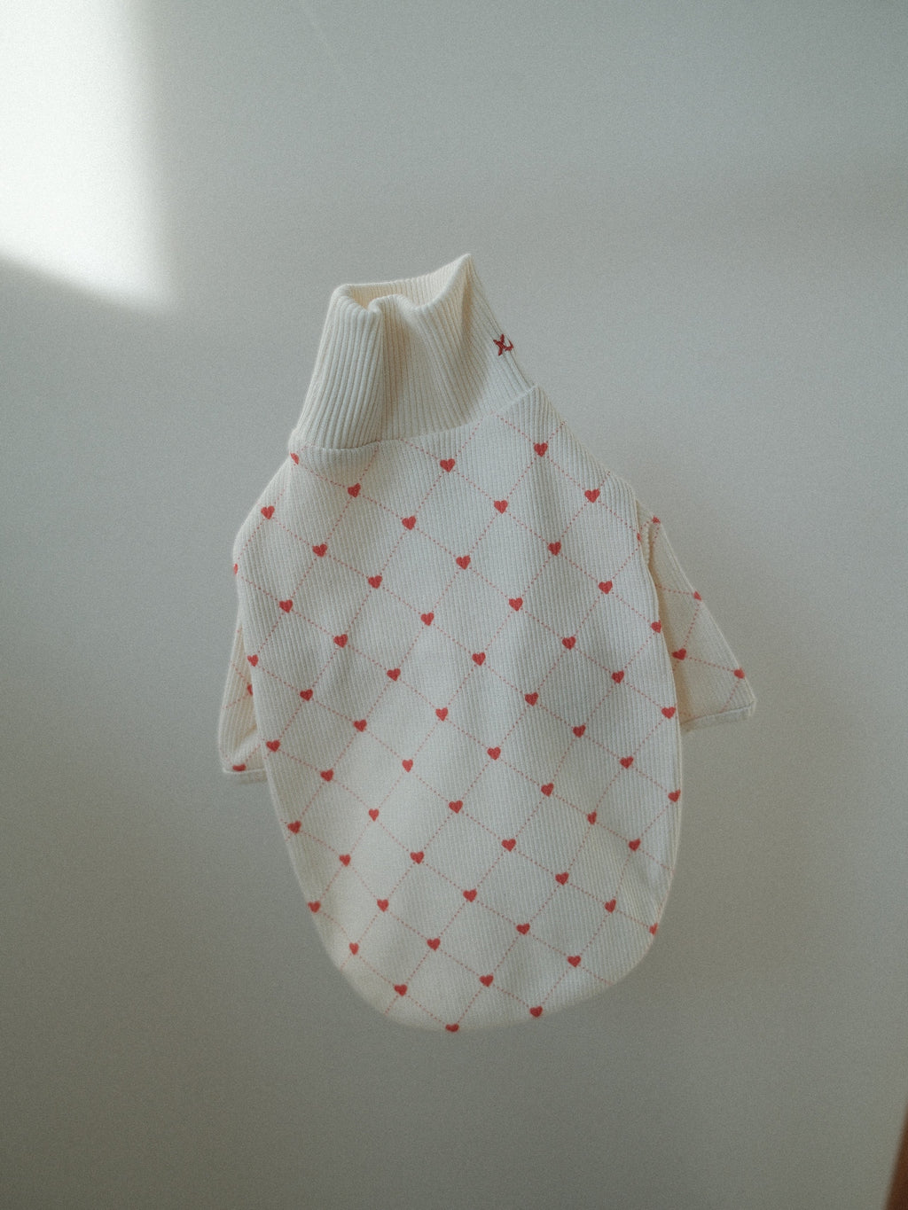 White dog sweater with red heart pattern on a light gray background