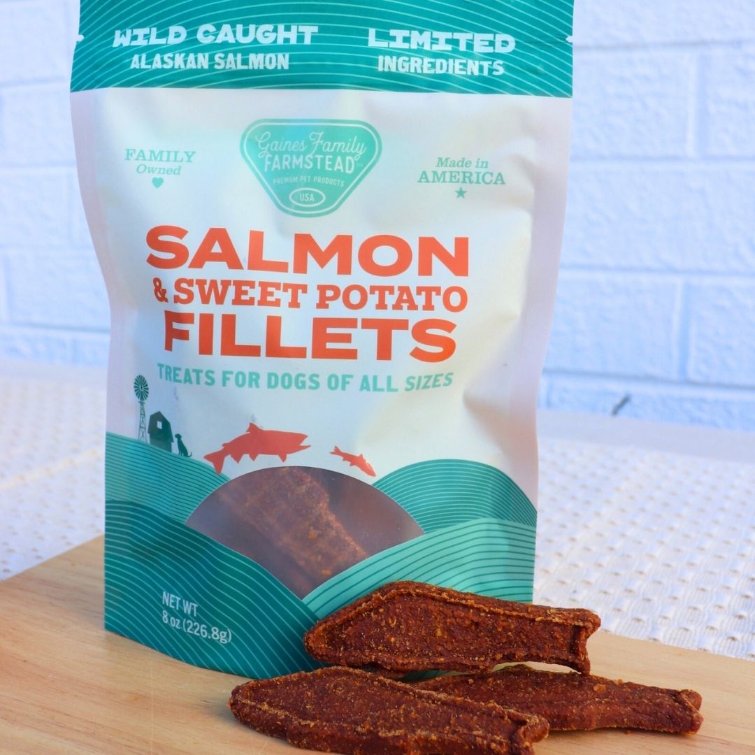 Package of Salmon & Sweet Potato Fillets for dogs with two fillets in front on a wooden surface.