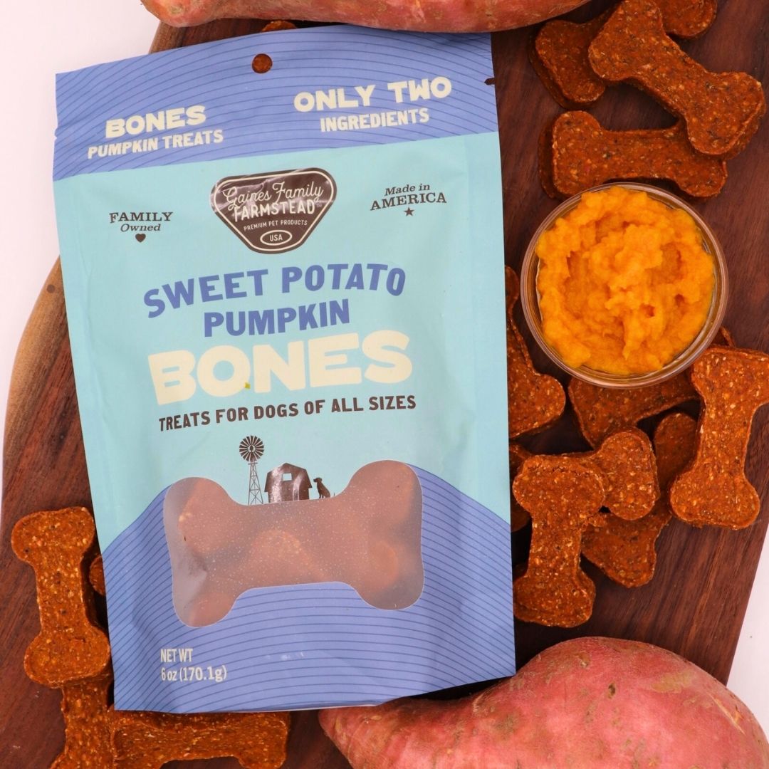 Package of 'Sweet Potato Pumpkin Bones' dog treats with a bowl of treats and more bones on a wooden surface.