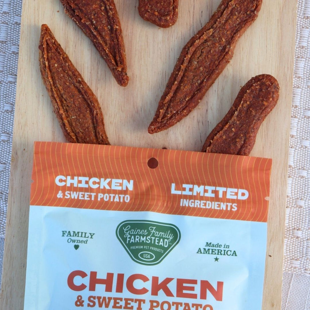 Dried chicken and sweet potato treats on a wooden board with a Gaines Family Farmstead package.