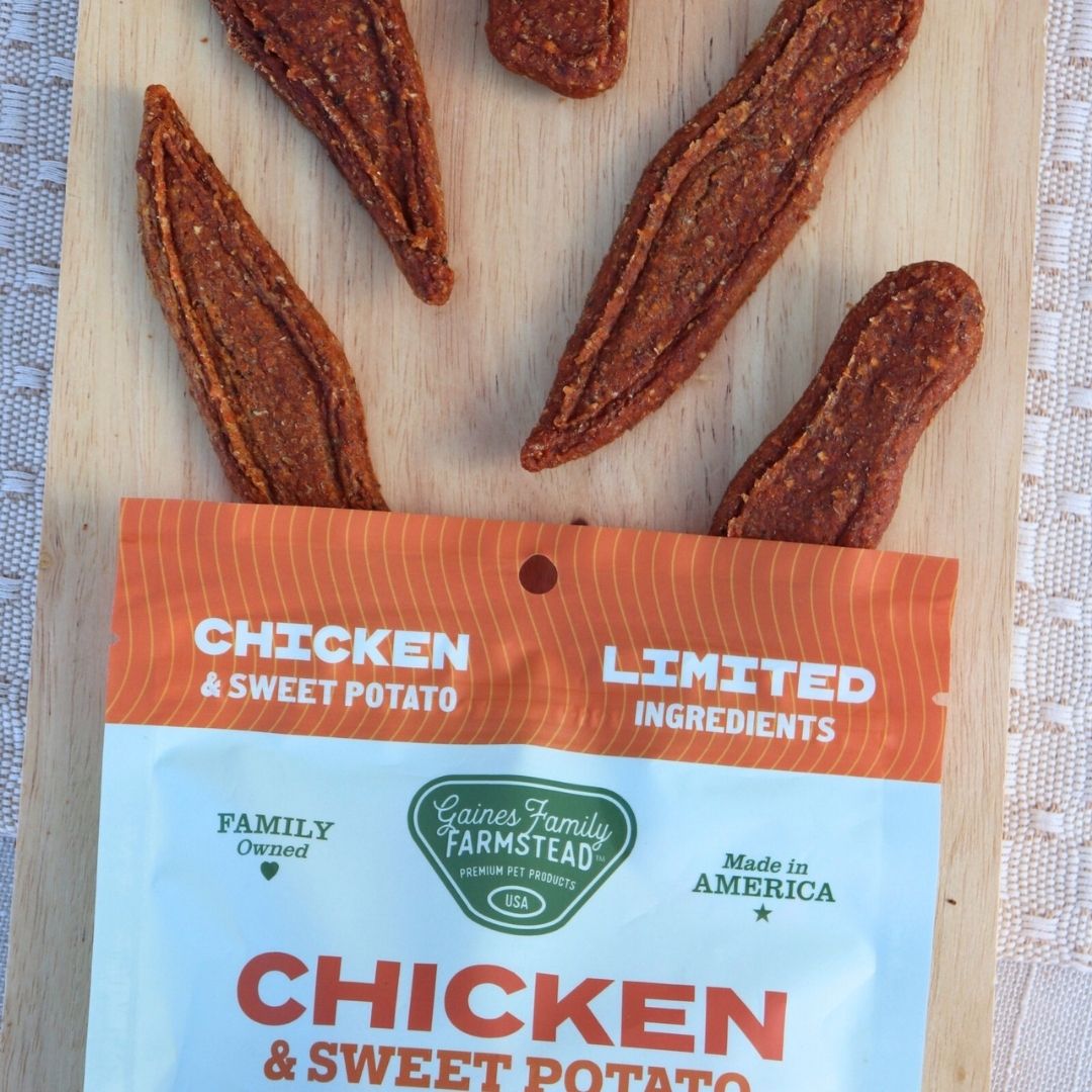 Dried chicken and sweet potato treats on a wooden board with a Gaines Family Farmstead package.