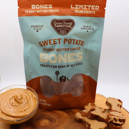 Package of Gaines Family Farmstead Sweet Potato Peanut Butter Coated Bones for dogs on a wooden surface with treats.