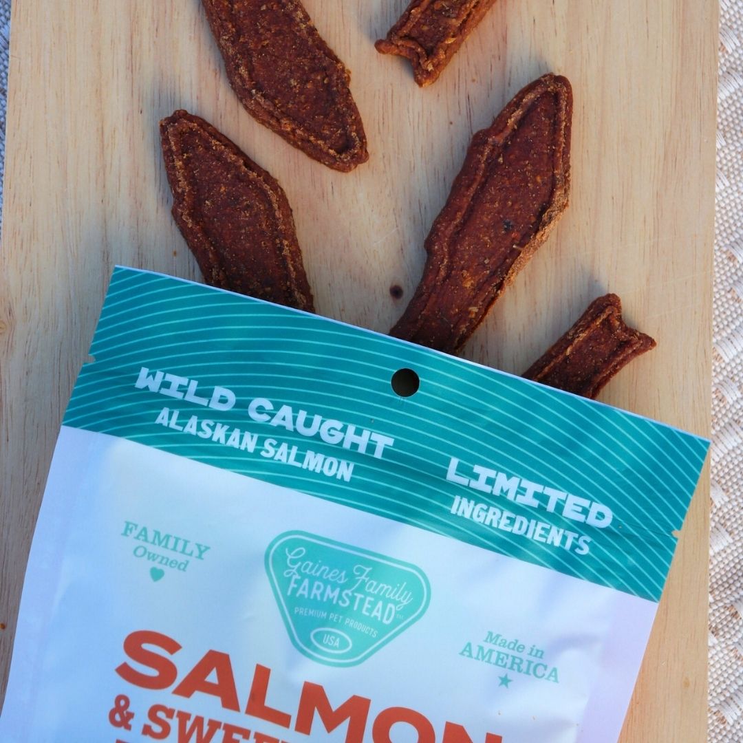 Salmon jerky on a wooden board with a package labeled 'Wild Caught Alaskan Salmon' from Gaines Family Farmstead.