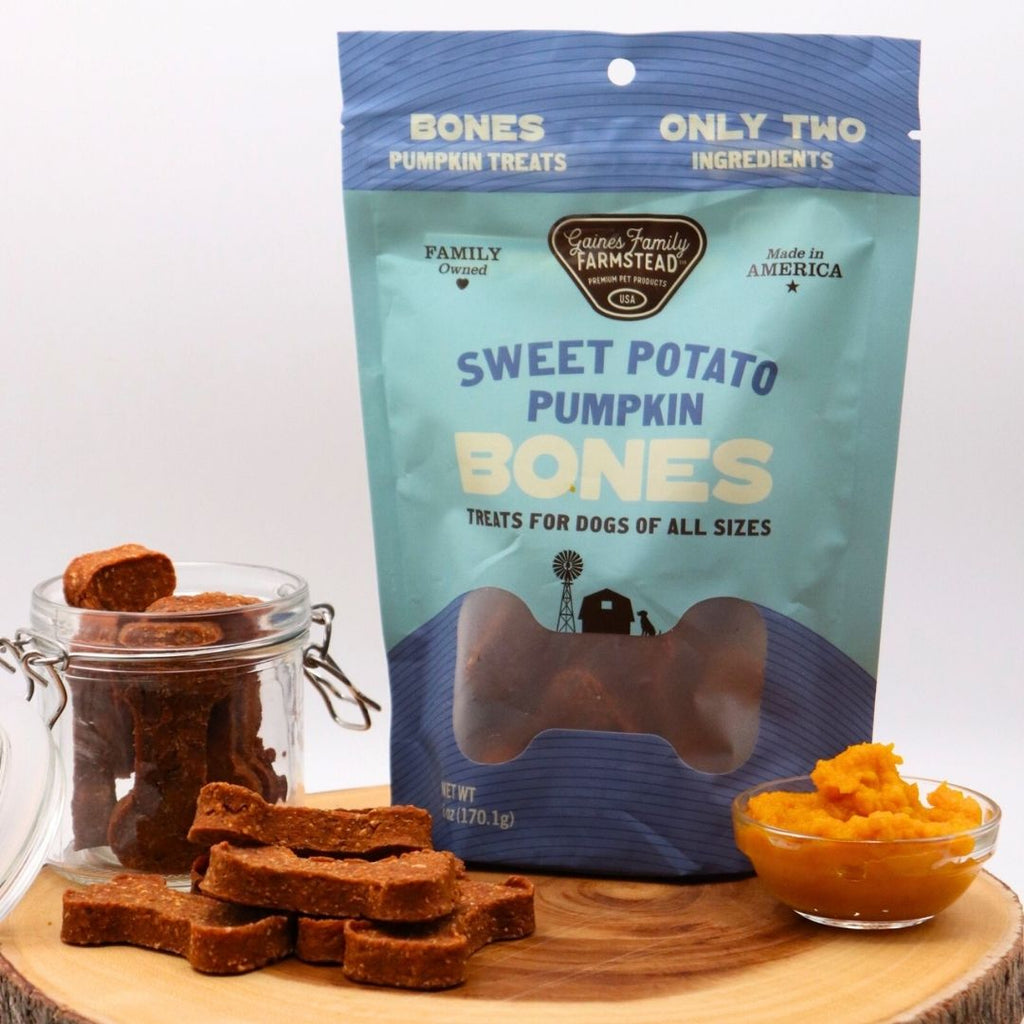 Bag of 'Sweet Potato Pumpkin Bones' dog treats with treats and pumpkin puree on a wooden board.