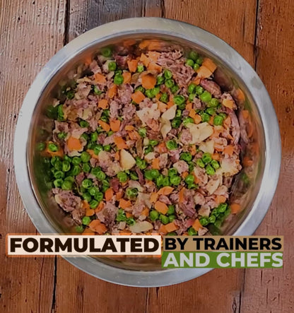 Dog food mix with vegetables in a bowl on a wooden surface, labeled 'Formulated by Trainers and Chefs'.