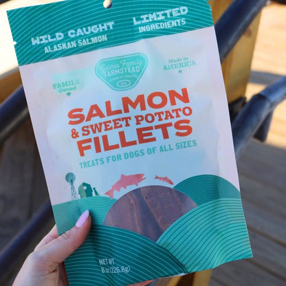Package of salmon and sweet potato fillets for dogs held by a hand.