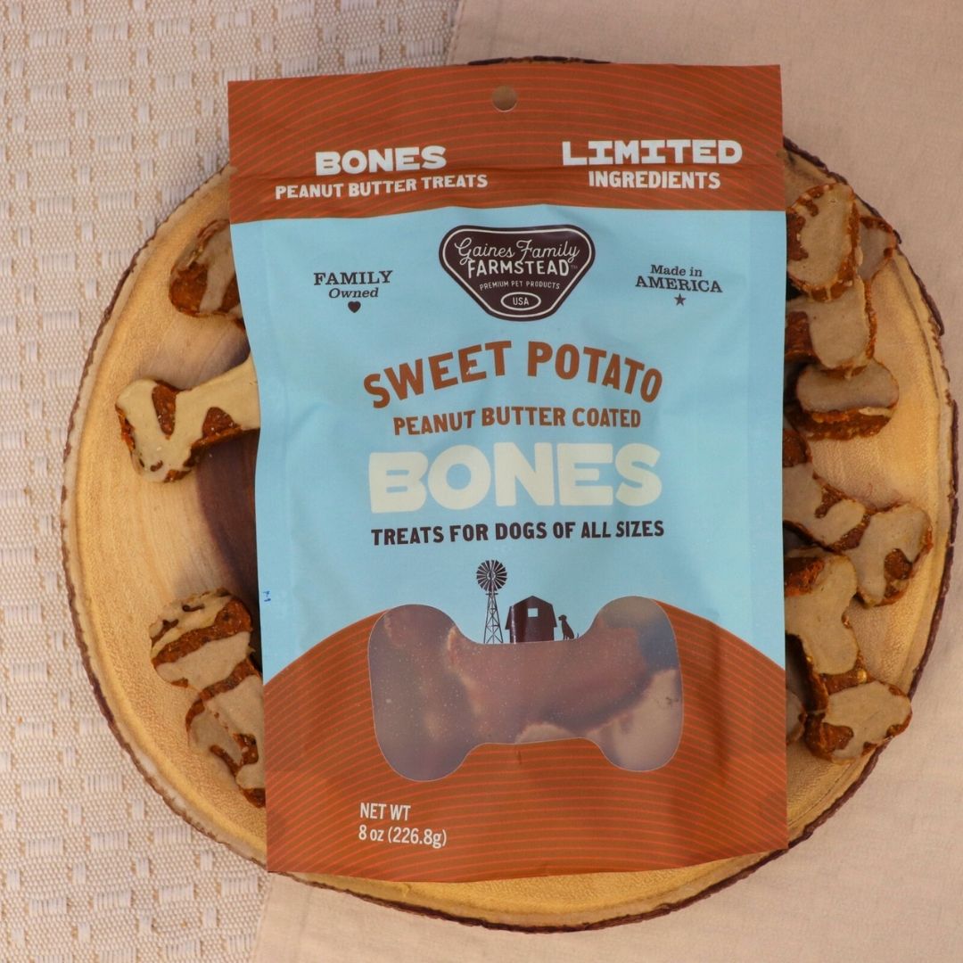 Package of 'Sweet Potato Peanut Butter Coated Bones' dog treats on a wooden board with treats.