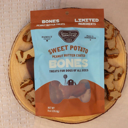 Package of 'Sweet Potato Peanut Butter Coated Bones' dog treats on a wooden board with treats.