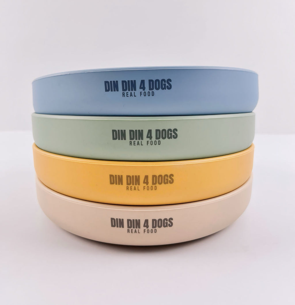 Stack of four dog bowls in different colors with 'DIN DIN 4 DOGS' branding on a light gray background.