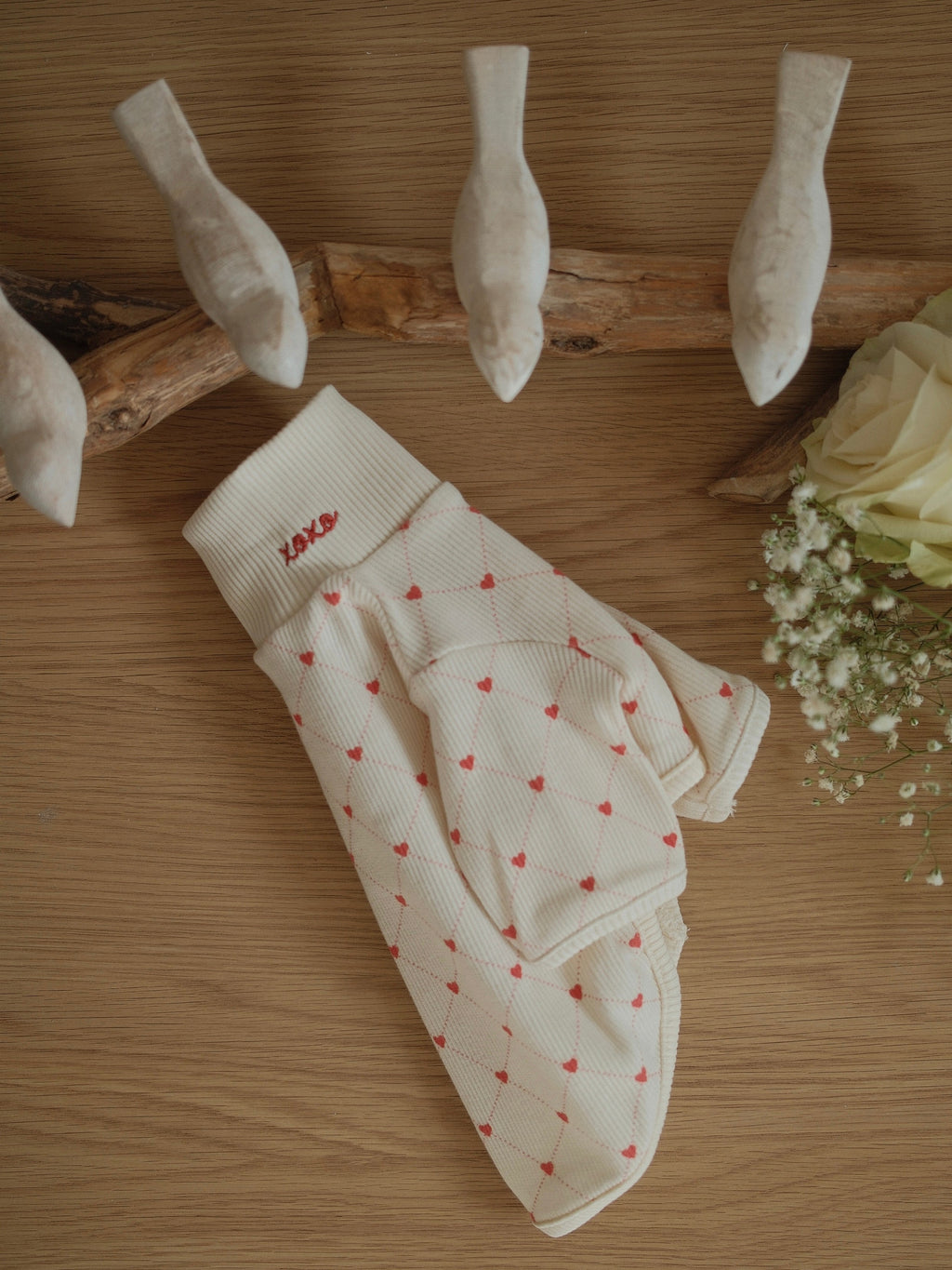 pet sweater with heart patterns on a wooden surface with flowers and sticks.
