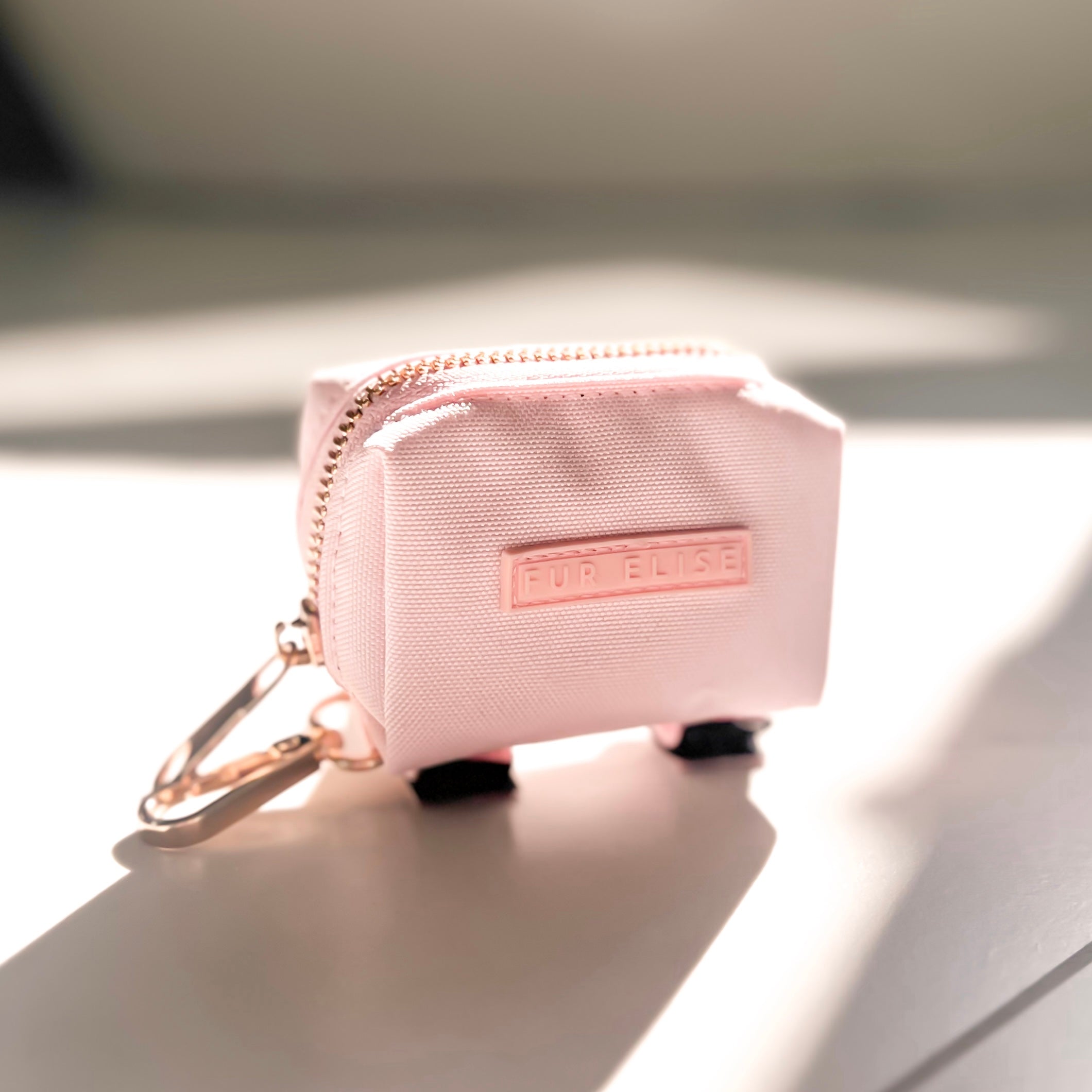 Pink keychain pouch with a brand logo on a reflective surface