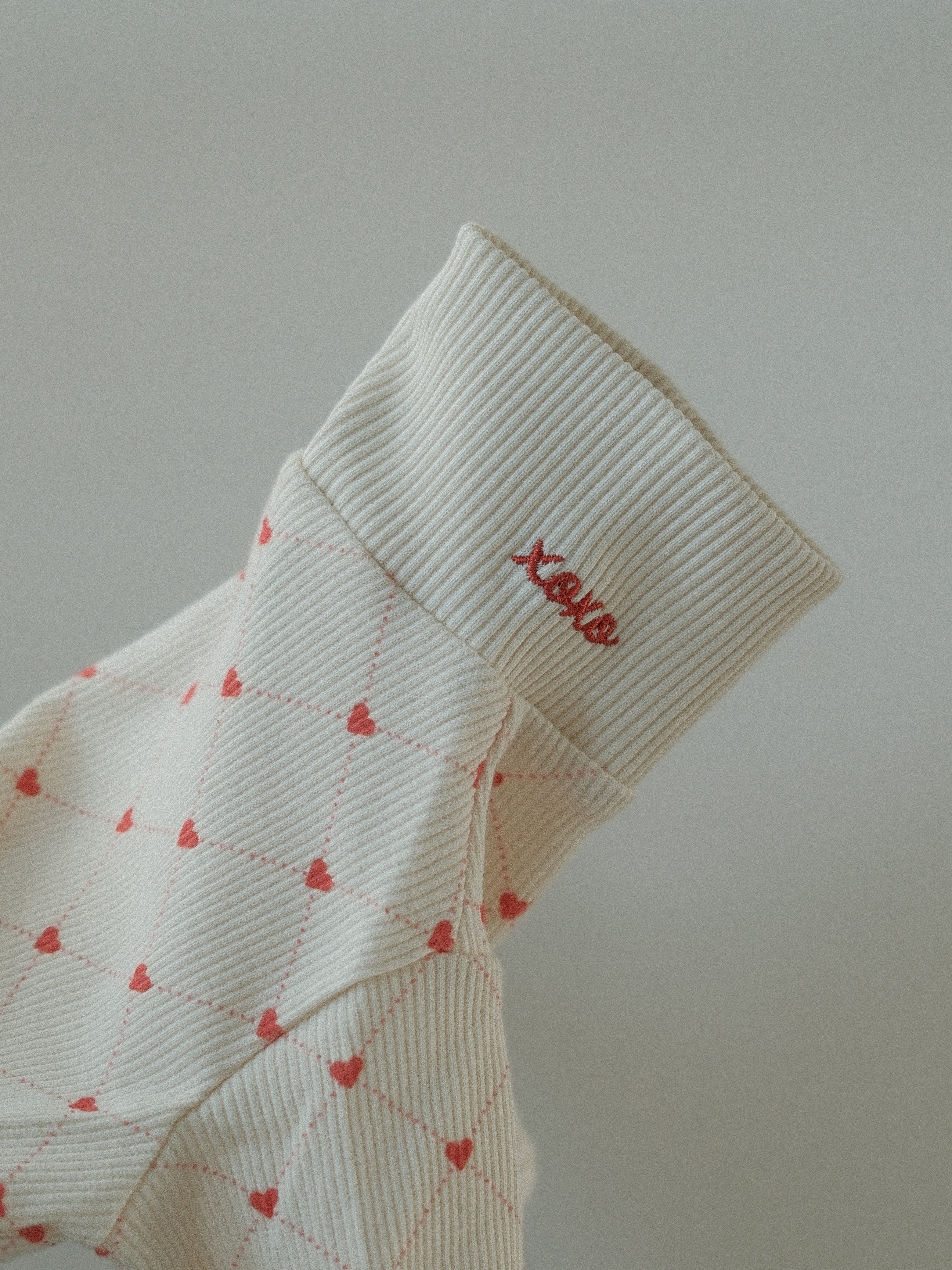 White dog sweater red heart patterns and 'XOXO' text on a light gray background