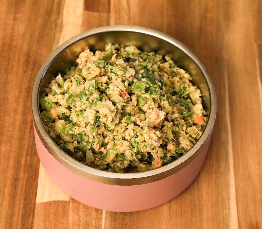 Pink pet food container filled with a mix of vegetables and meat on a wooden surface