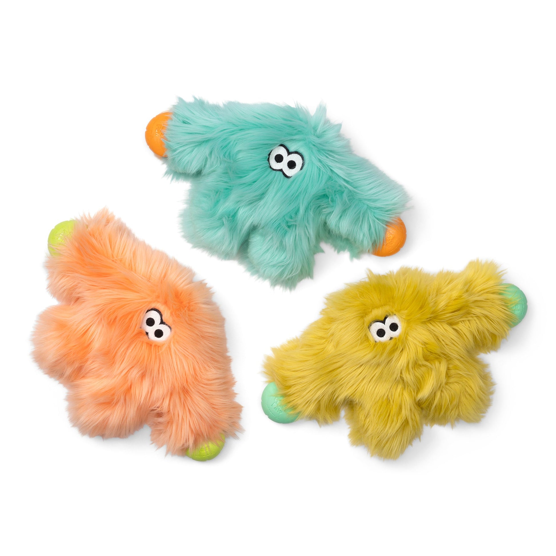 Three fuzzy monster-shaped dog toys in mint green, peach, and yellow, each with small orange paws/feet and light green/blue-green claws, shown on a white background.