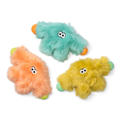 Three fuzzy monster-shaped dog toys in mint green, peach, and yellow, each with small orange paws/feet and light green/blue-green claws, shown on a white background.