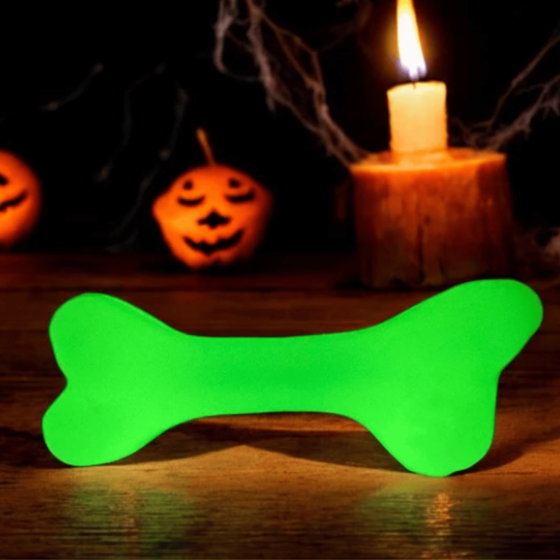 Green bone-shaped glow stick on a wooden surface with Halloween decorations in the background.