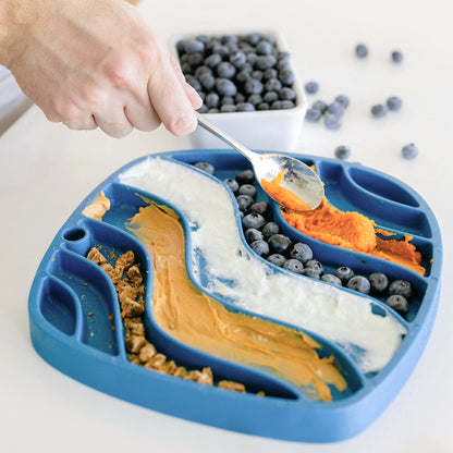 Blue divided plate with various food items and a hand using a spoon.