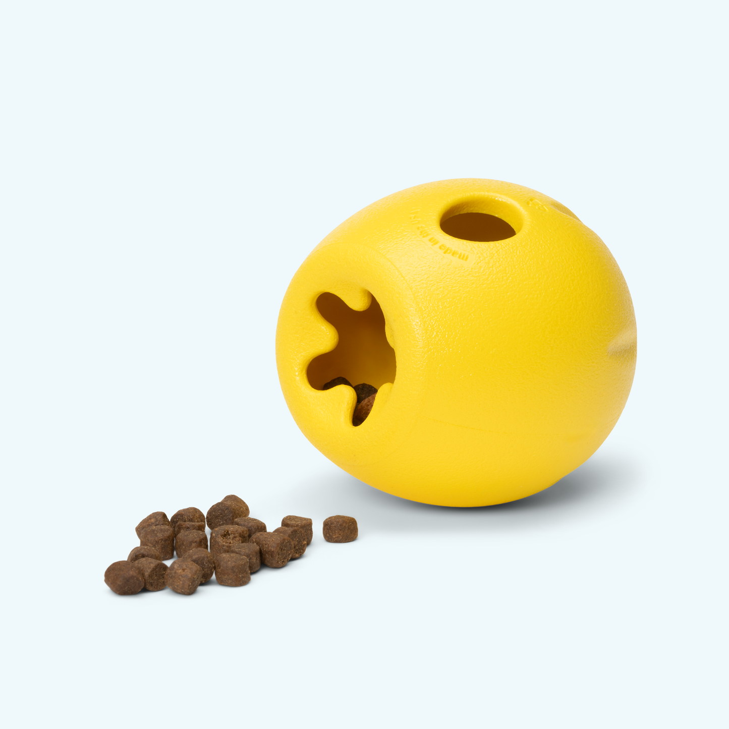 Yellow ball-shaped pet toy with a puzzle cutout and scattered treats on a white background