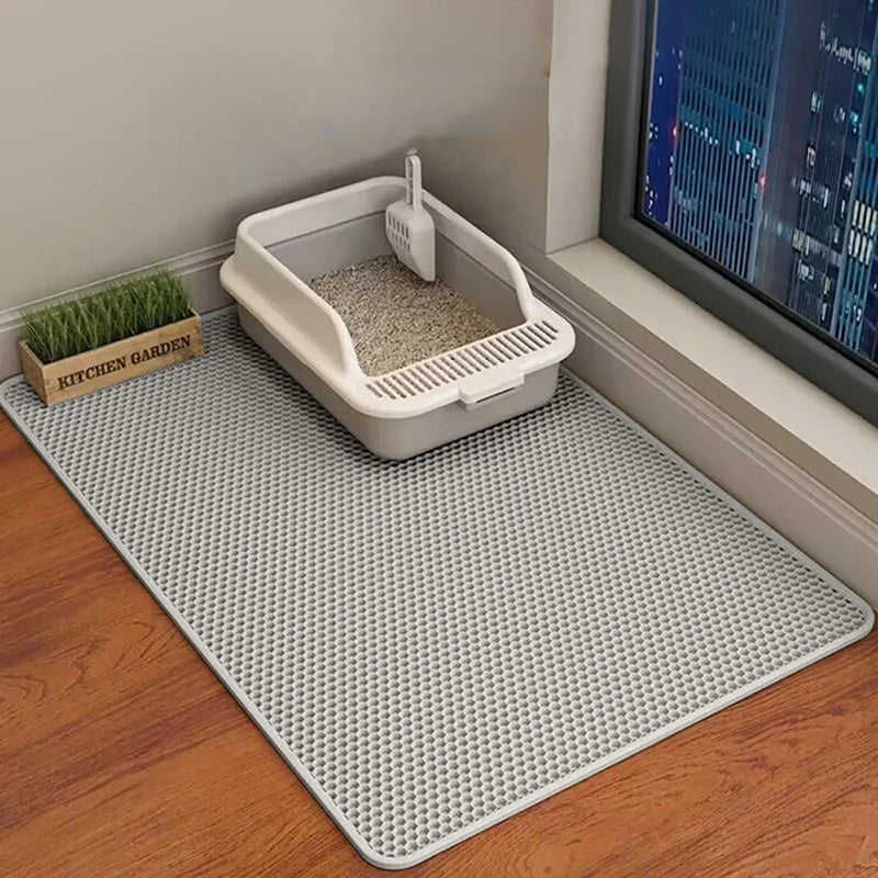 Cat litter box on a black mat with a view of a cityscape through a window.