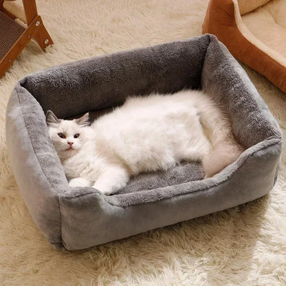 White cat lying on a gray pet bed in a cozy room.