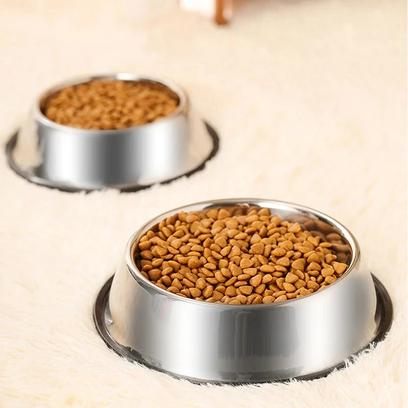 Two metal bowls filled with pet food on a wooden floor.