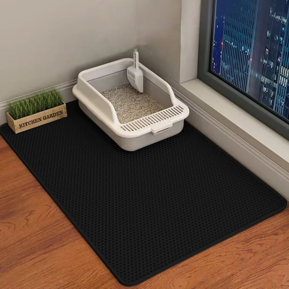 Cat litter box on a black mat with a view of a cityscape through a window.