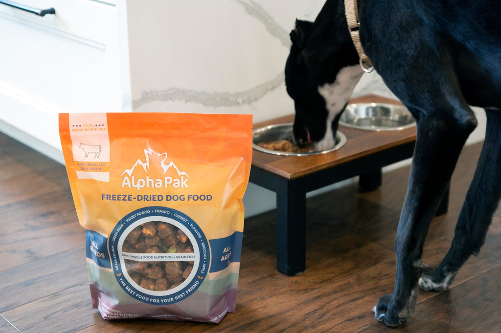 Alpha Pak freeze-dried dog food package with a dog eating from a bowl in the background.