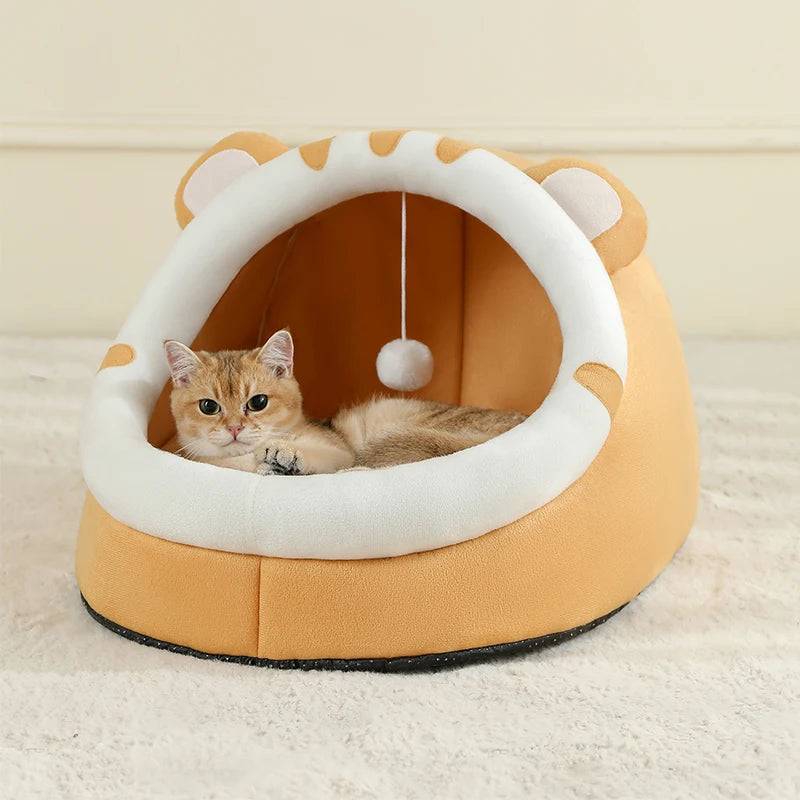 Cat lying inside a yellow and white cat bed with a hanging toy on a light background