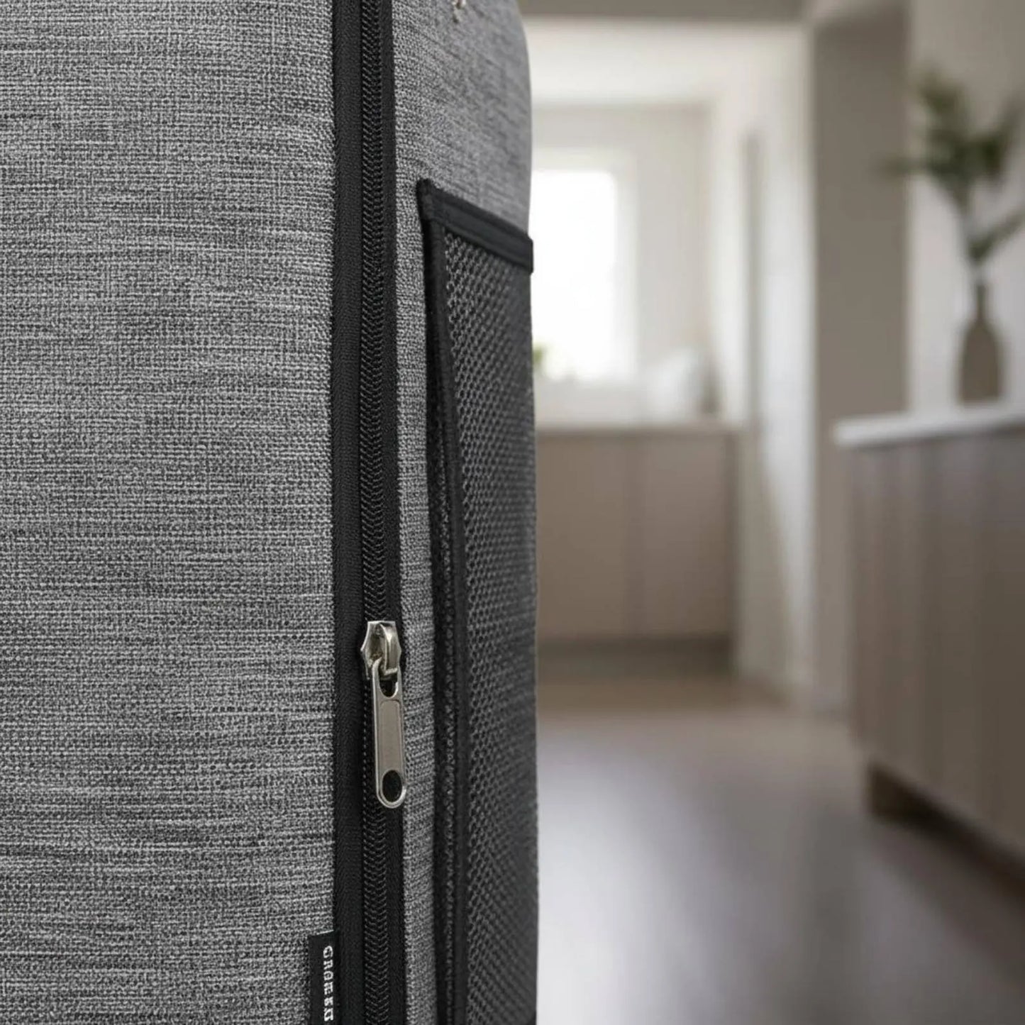 Close-up of a textured gray suitcase with a zipper, blurred indoor background
