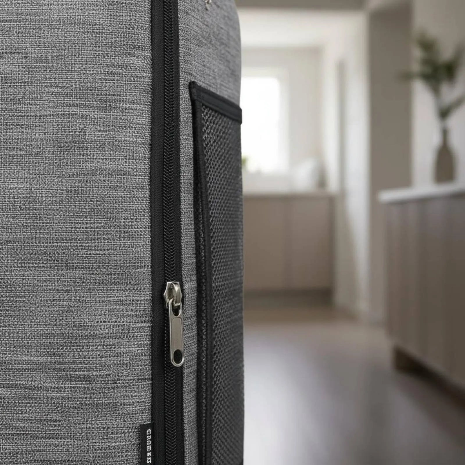 Close-up of a textured gray suitcase with a zipper, blurred indoor background