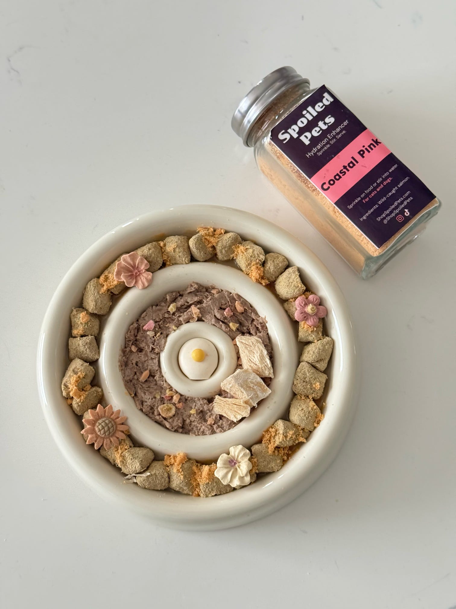 Dog treat bowl with treats arranged in a circular pattern, next to a jar labeled 'Spoiled Pets' on a white background.