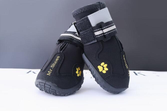 Pair of black dog boots with yellow paw prints on a white surface.