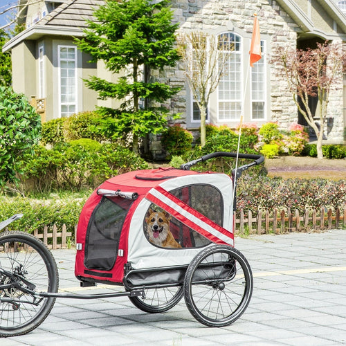 Red and white pet bike trailer with a dog inside, parked on a driveway in front of a house.