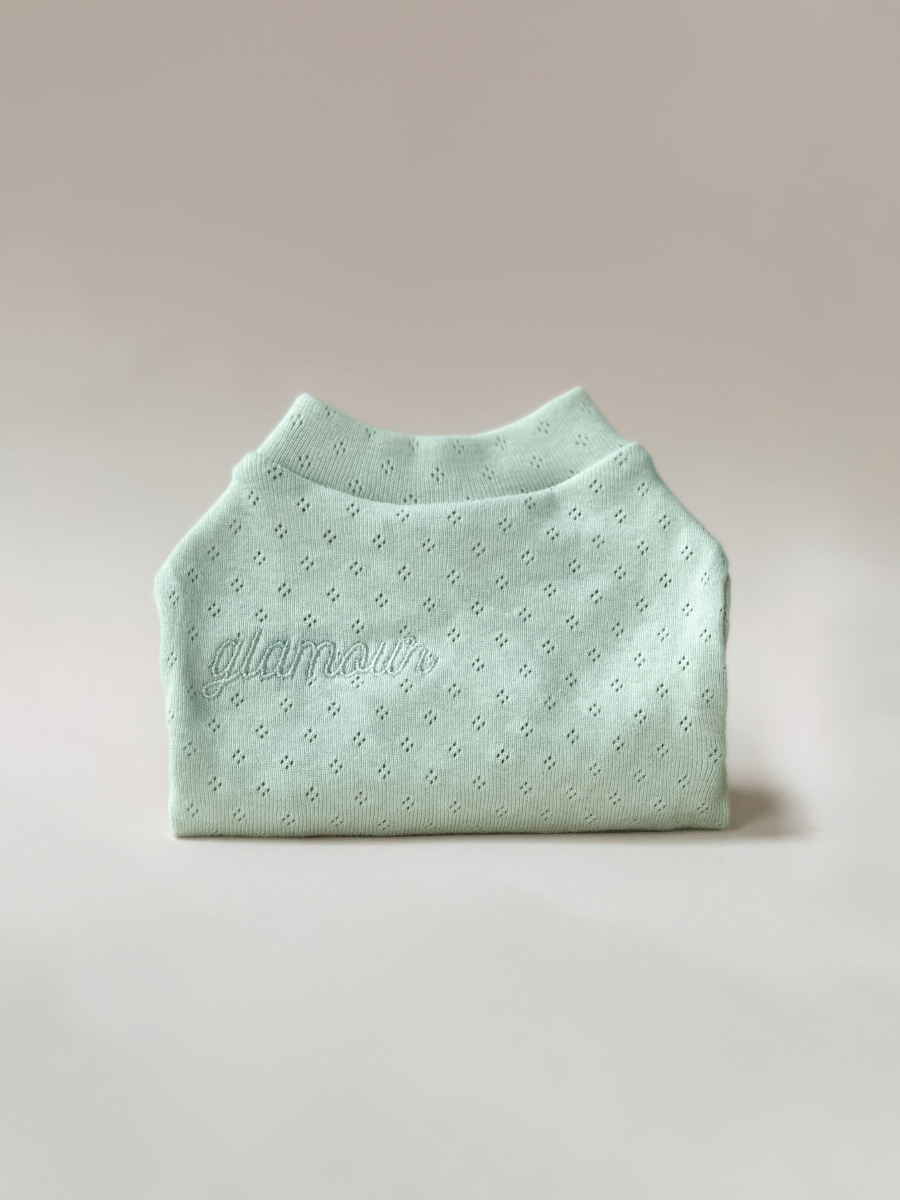 Folded light green sweater with 'damir' branding on a beige background