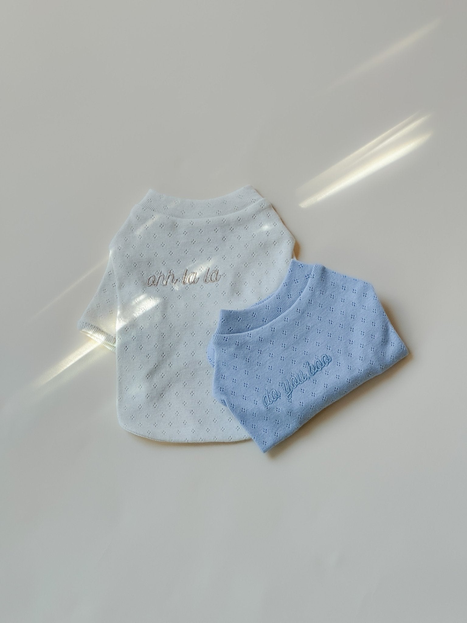 Gray bib with 'hello baby' text and blue bib with 'love' text on a light gray background